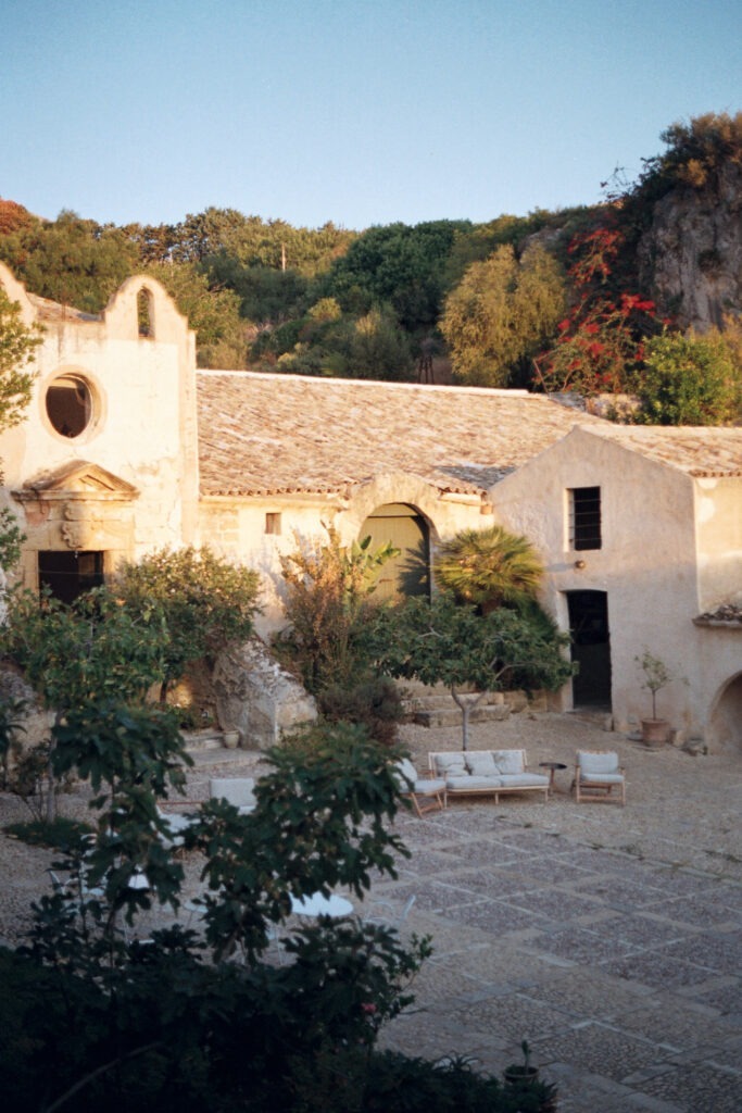 Secluded white stone house on Mediterranean hillside surrounded by lush greenery.