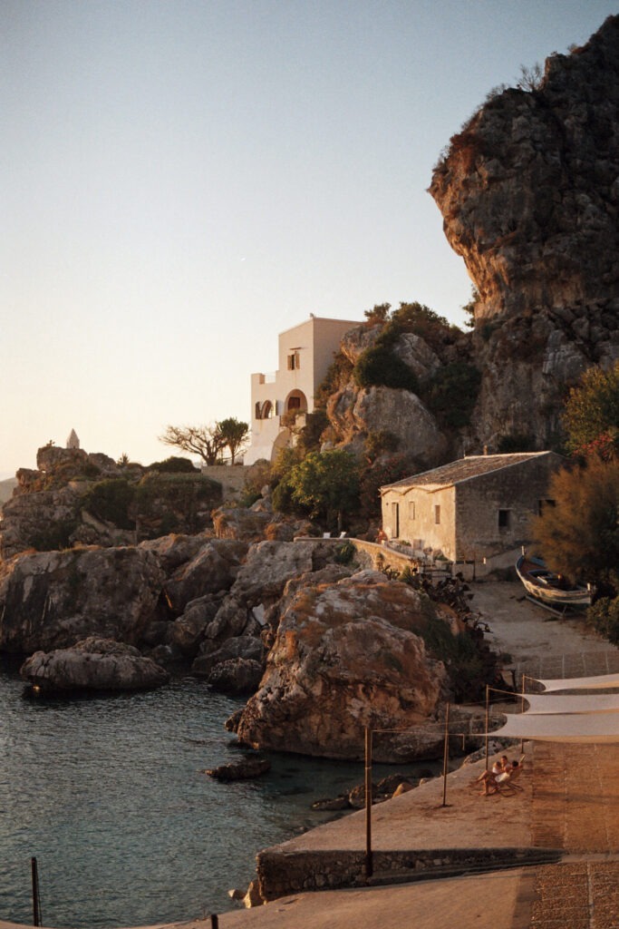 Mediterranean coastal village at sunset, capturing stone houses nestled against rocky cliffs