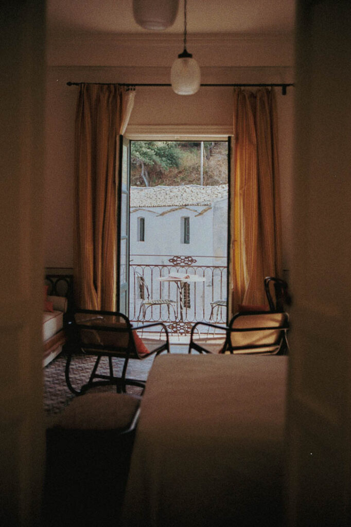 Interior of a cozy room with an open door leading to a balcony overlooking a picturesque building.