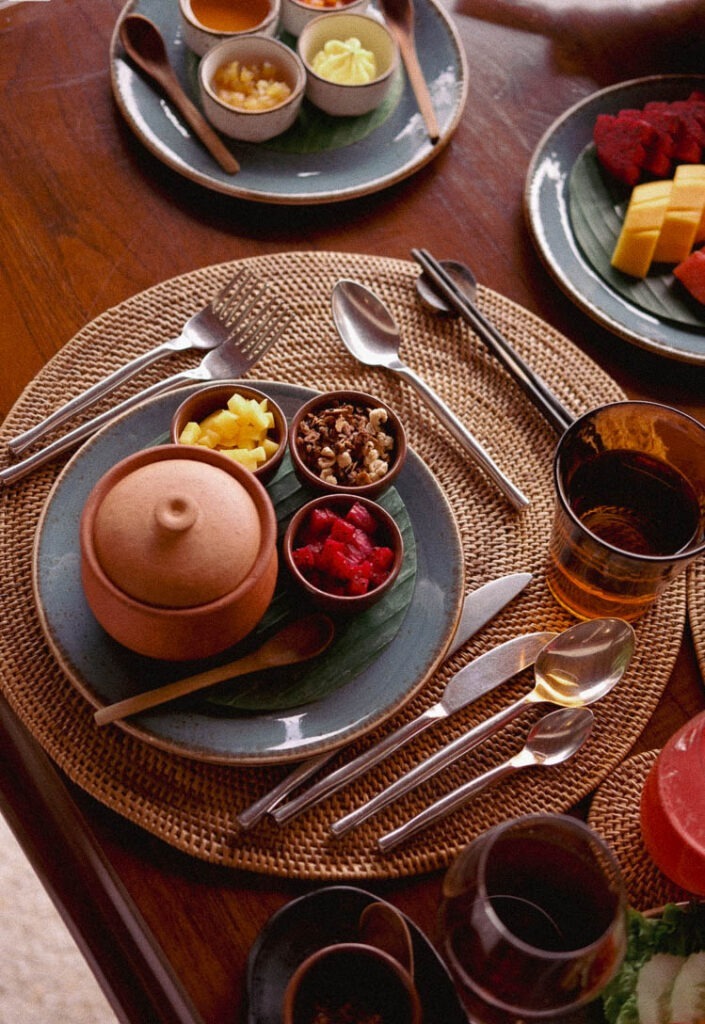 Luxurious breakfast setting at Belmond La Residence, Phou Vao, Laos, featuring traditional ceramics and tropical fruit.