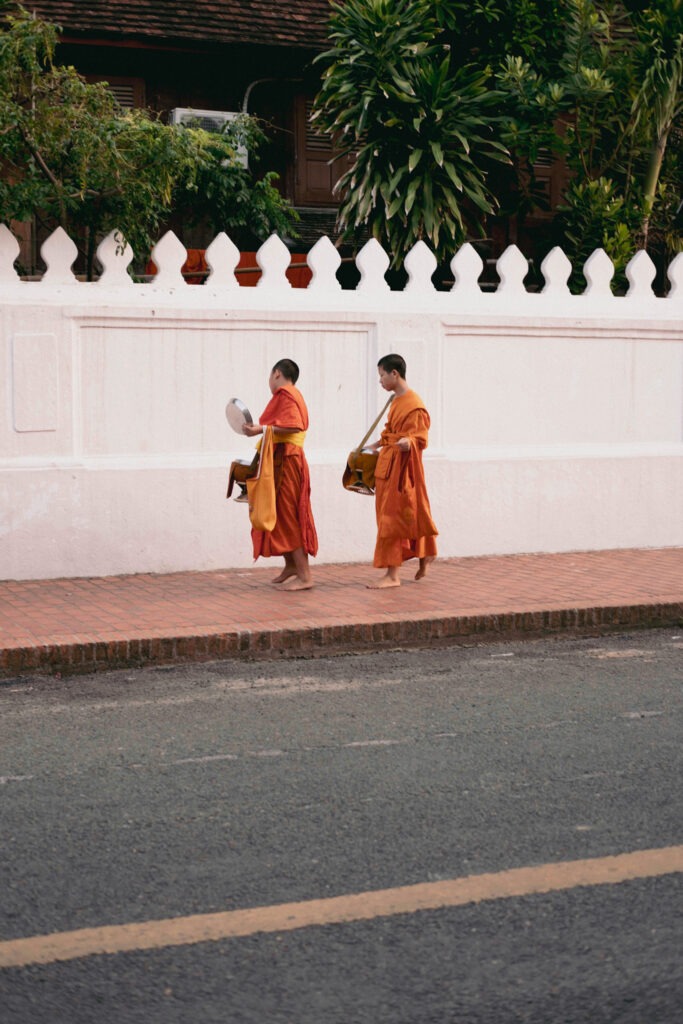 Two monks walking alongside a historic white wall in Luang Prabang, Laos